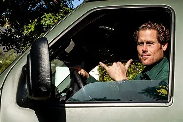 Eli Johnson at the wheel of the Johnson Tree Company van, in a green company shirt with the yellow tree mark on the chest.